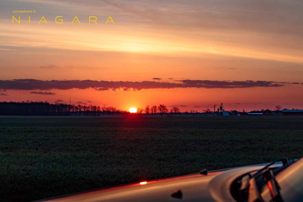 Sunrise over trees with a car in the foreground.